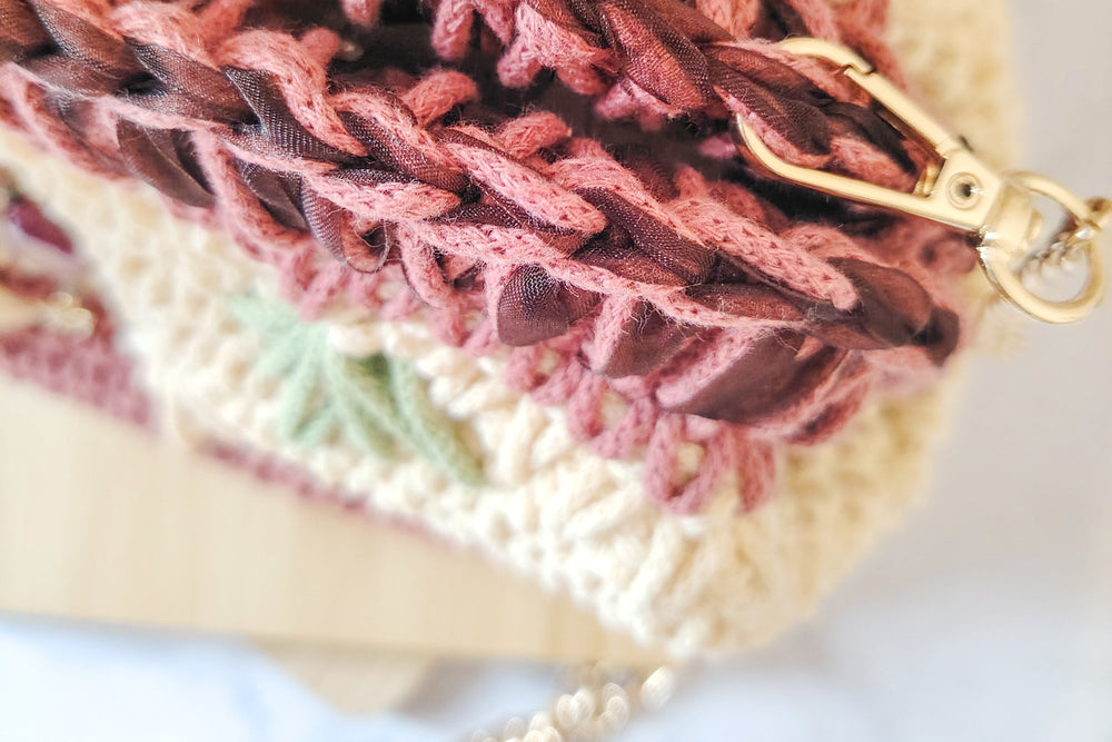 Gros plan sur le haut du sac au crochet. Fil rose et ruban bordeau
